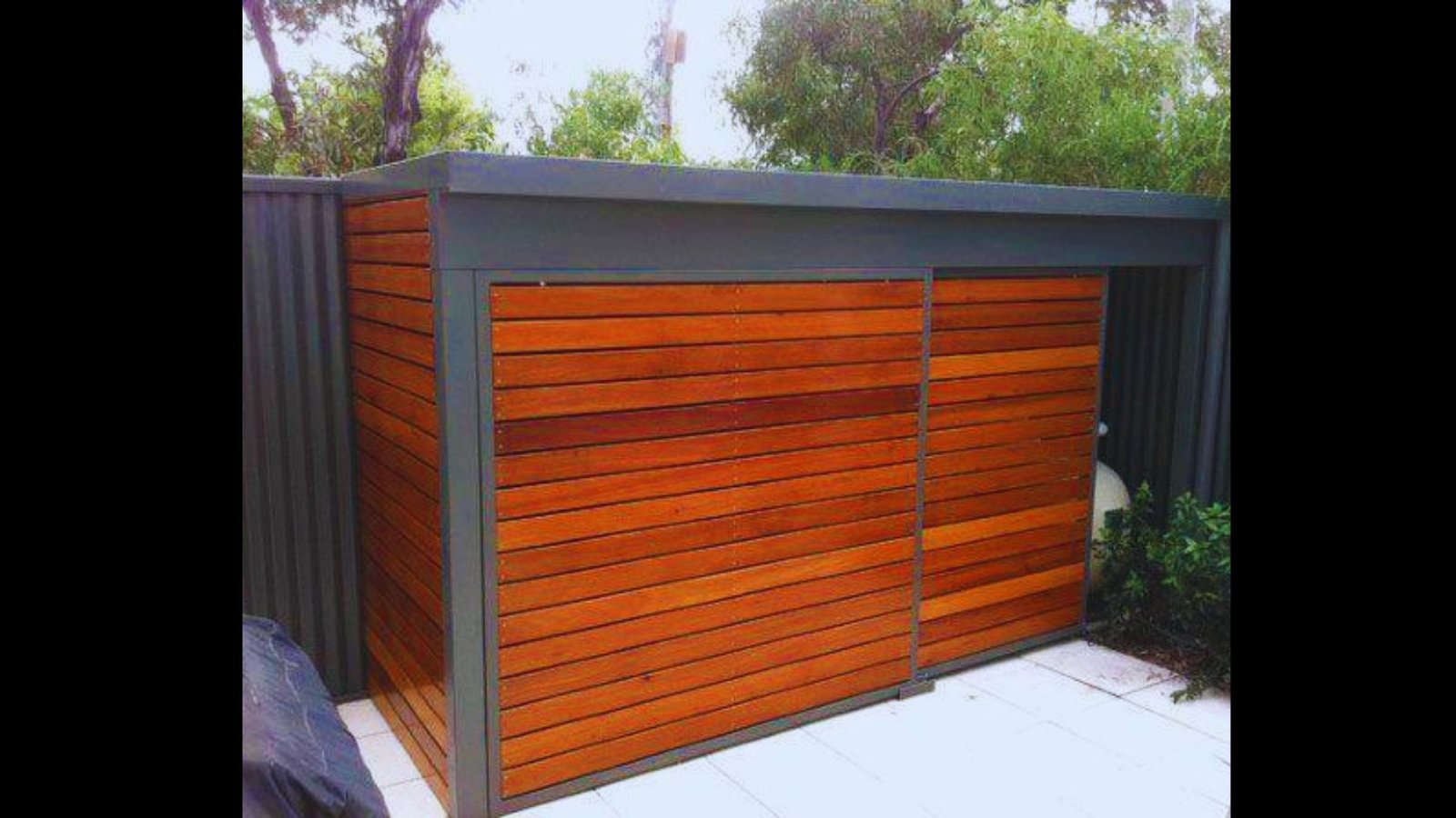 A coastal pool equipment shed with horizontal warm-toned timber cladding and dark metal frame framing.
