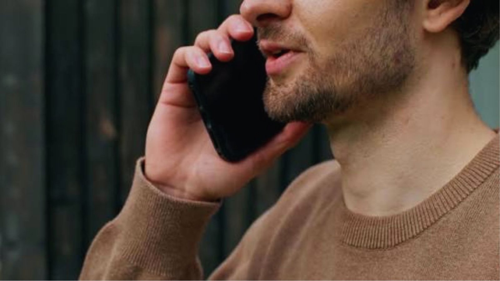 Close-up of a man in a tan sweater talking on a mobile phone held to his ear.