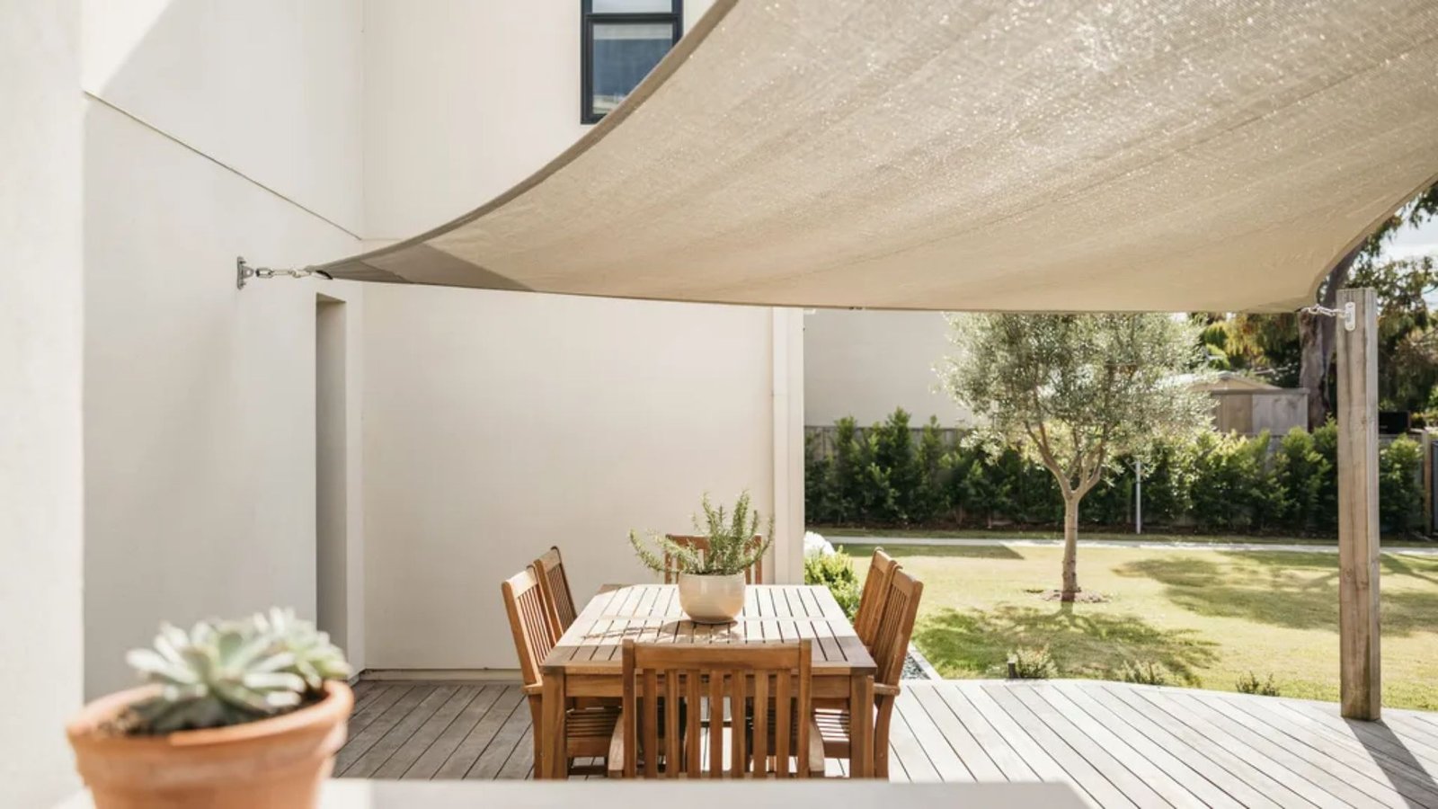 shade sail attached to a house wall and supported by wooden posts.