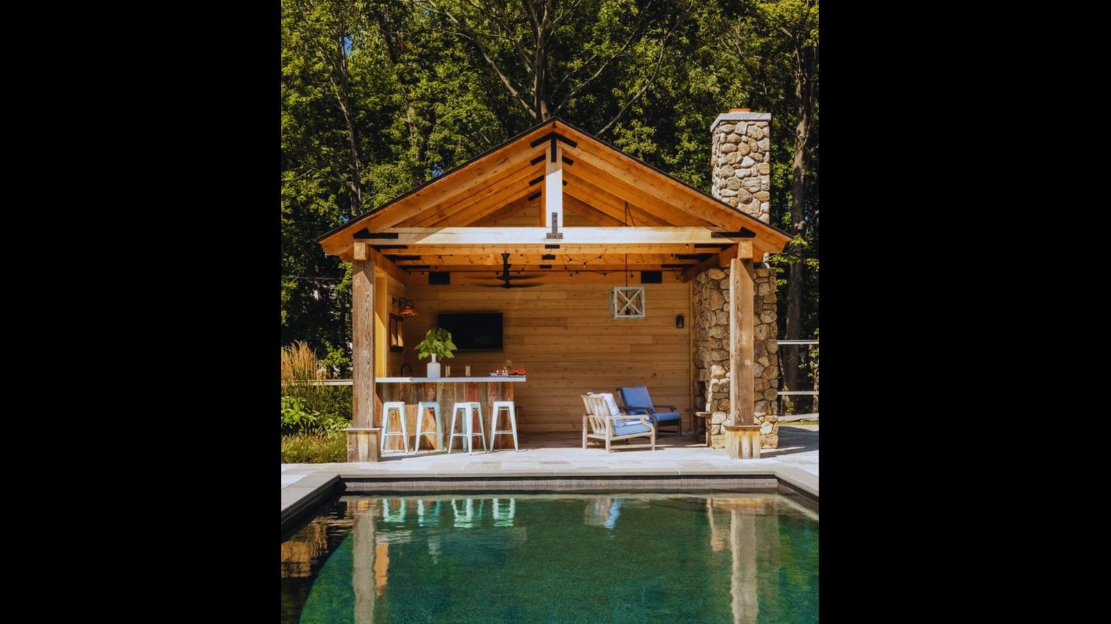 A stone and timber pool house structure with exposed wooden beams, stone pillars, and poolside lounge chairs.