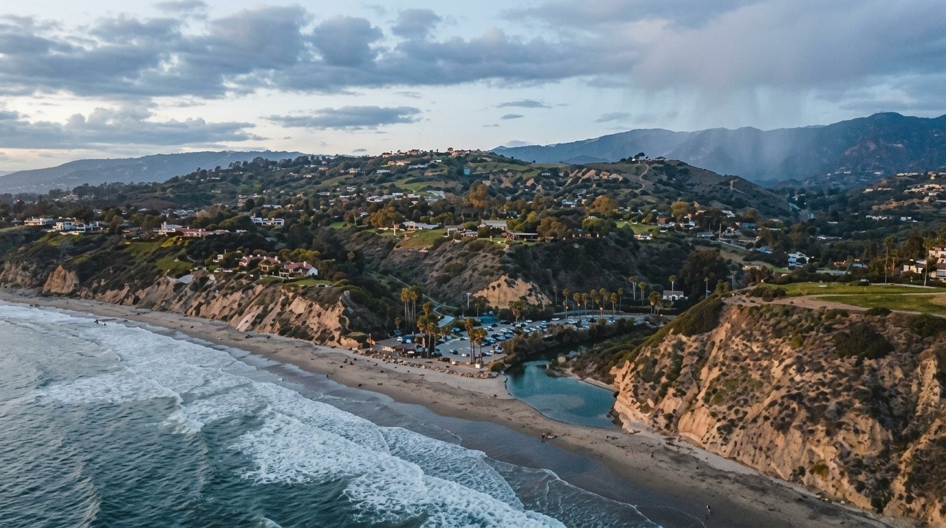 Aerial view of California coastal zone with cliffs, beach, ocean waves, hills, and homes.