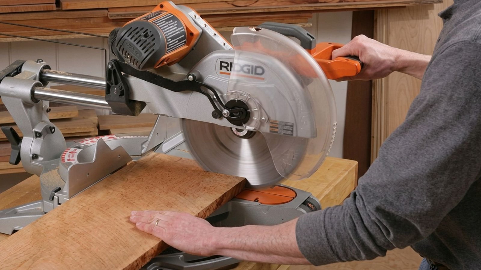 Man using a sliding miter saw to cut a wide wooden board on the workbench.