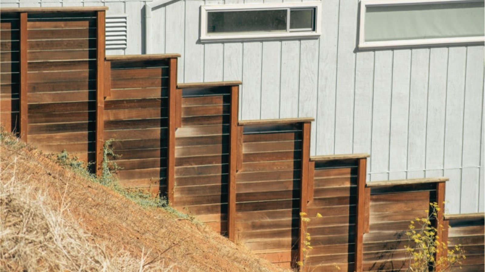 Stepped dark wood privacy fence on steep slope descending beside house