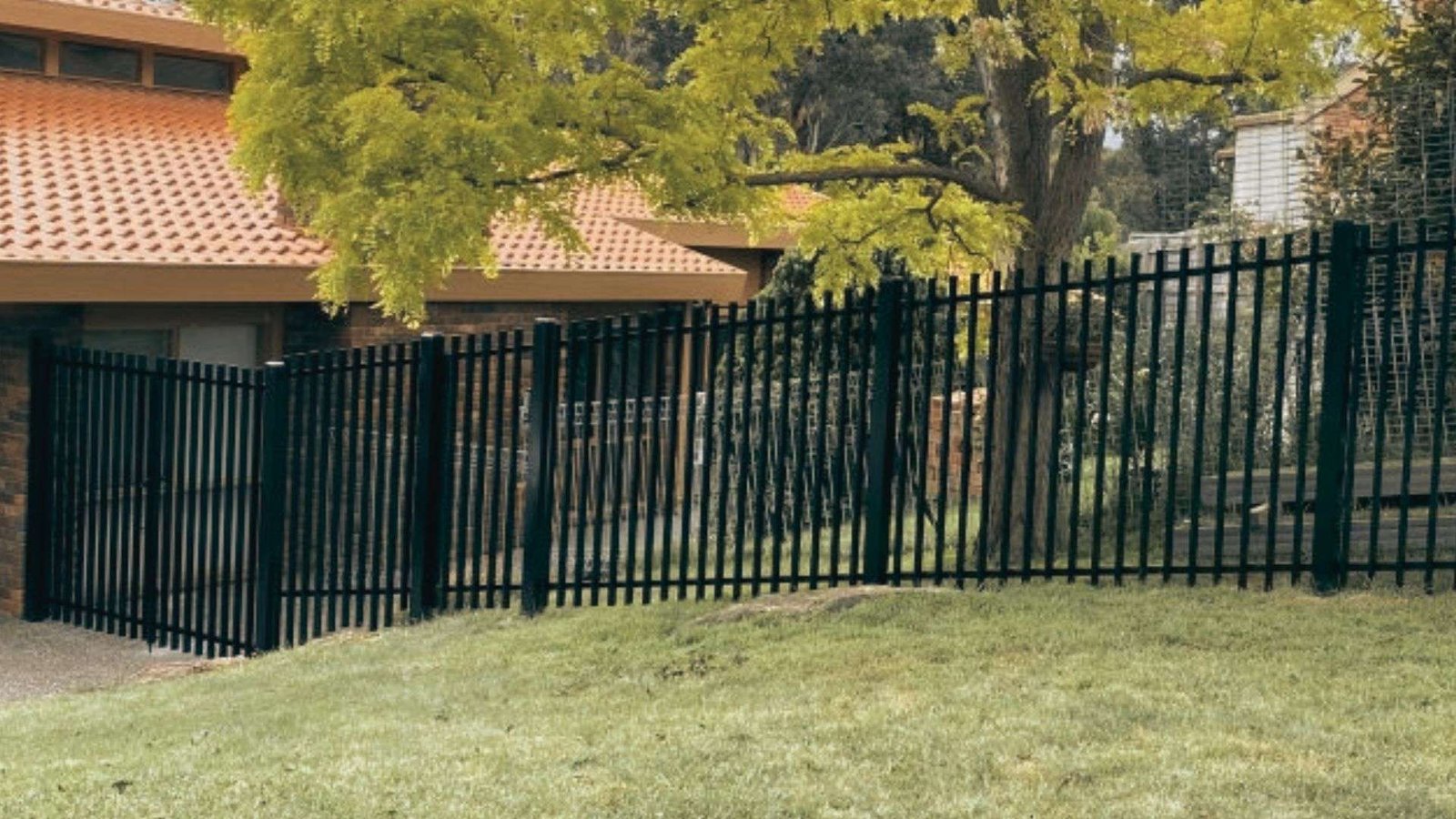 Black aluminum picket fence stepping down a sloped grassy yard in front of house