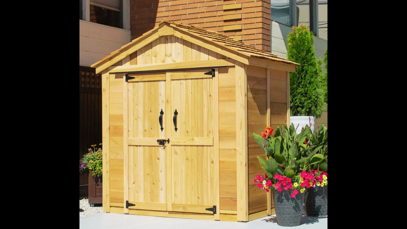 Light wooden pool equipment shed with double doors, black hardware, and a potted plant in front.