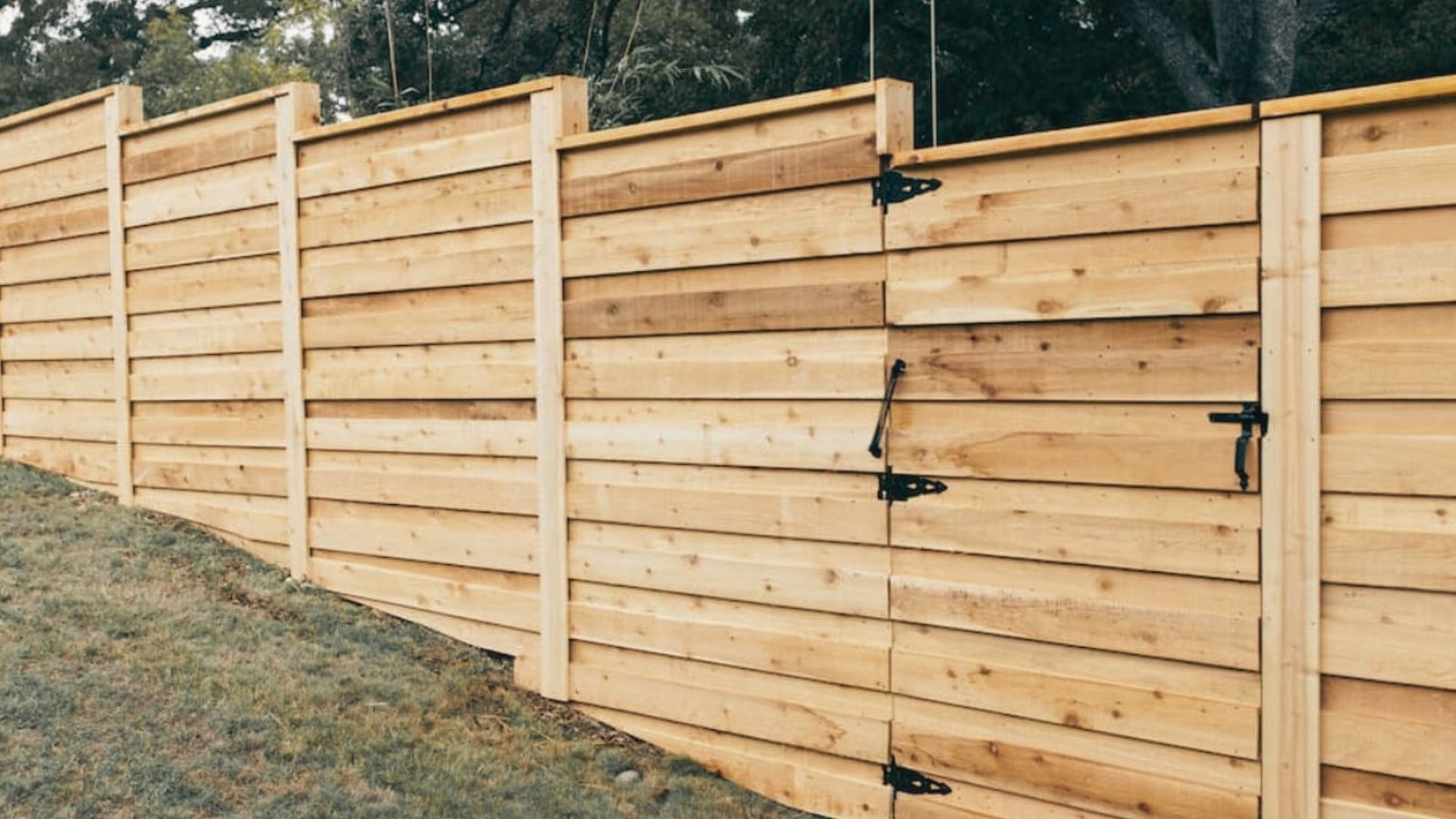 Wooden gate installed in step down fence on sloped yard with black hinges