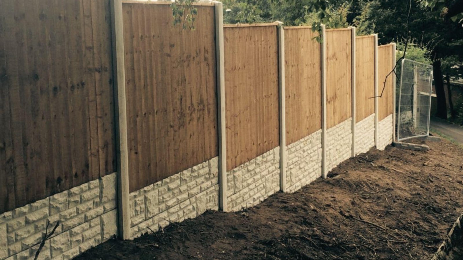 Wood fence with concrete posts and gravel boards stepping down a sloped dirt yard