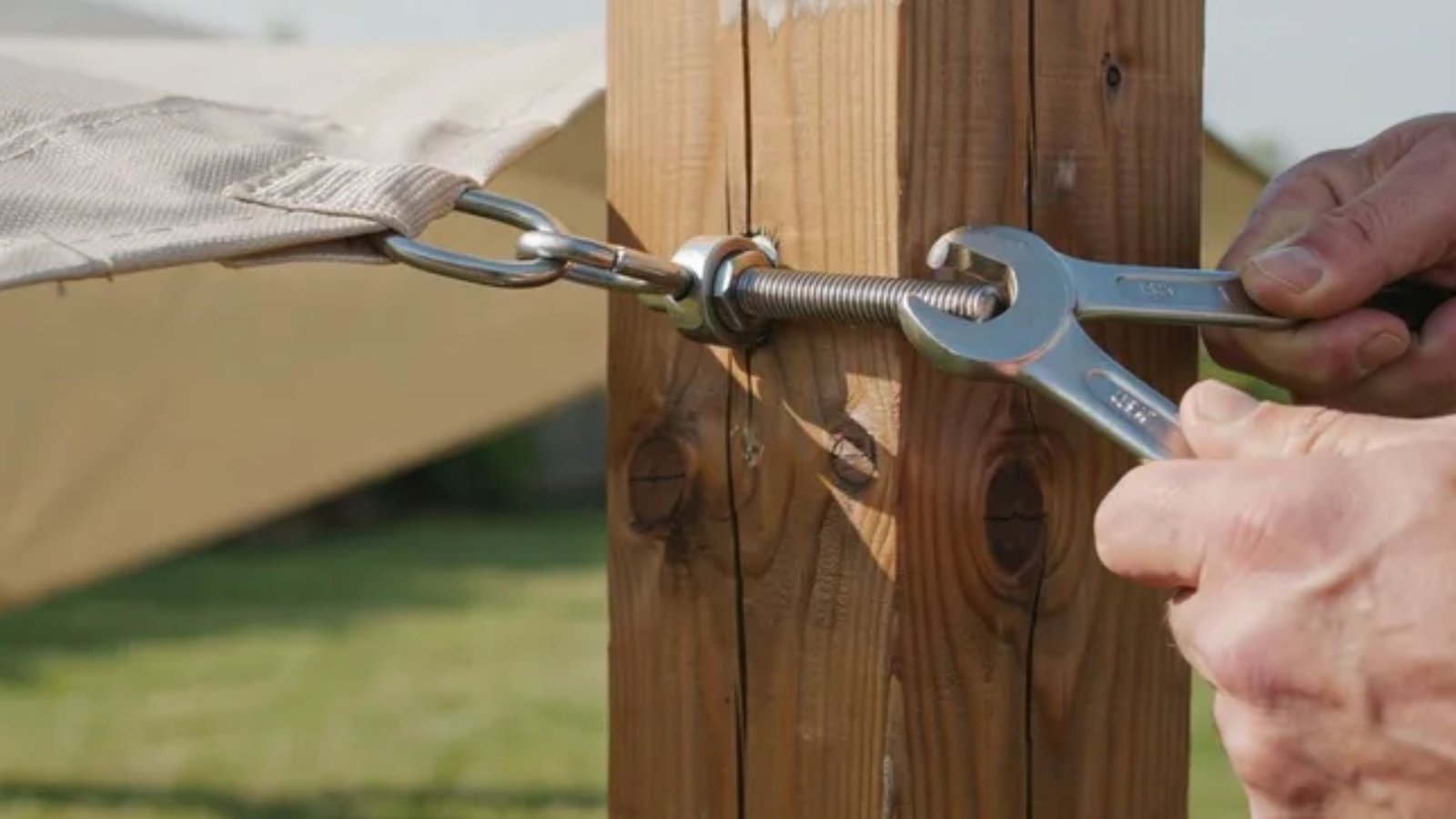tightening a shade sail turnbuckle on a wooden support post with a wrench.