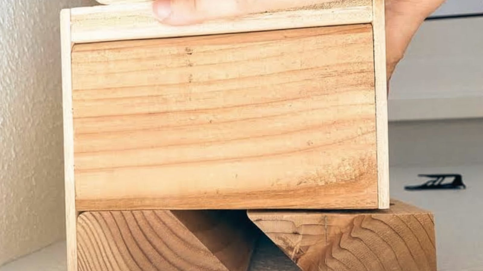 Hand holding a wooden panel with a french cleat mounted on an angled wall block.