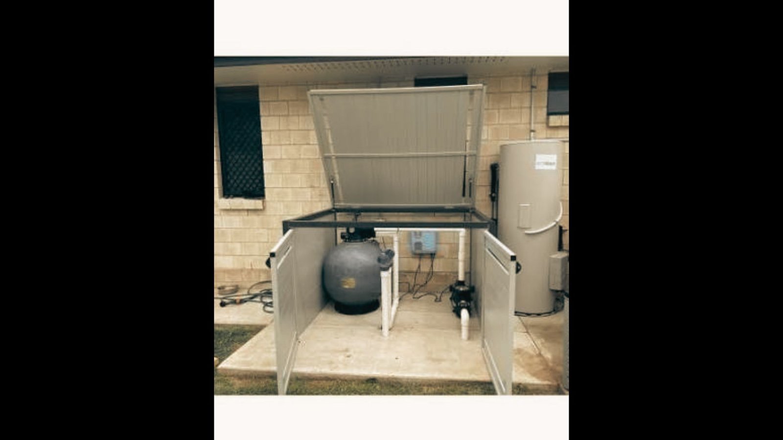 Built-in pool equipment cabinet attached to a stone wall with an open hinged top displaying pumps and filter.
