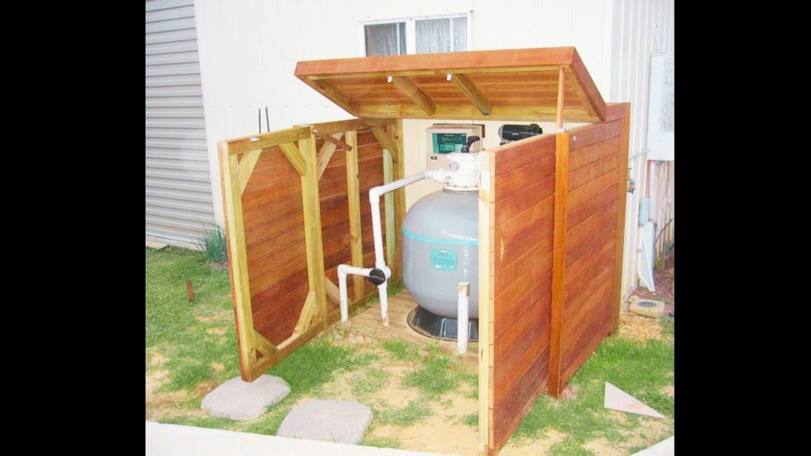 Wooden pool equipment enclosure with open hinged roof lid revealing pump and filter system.