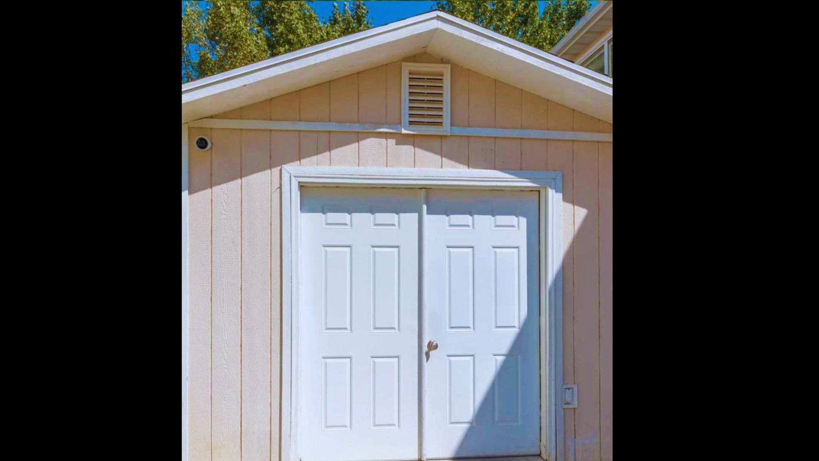 Wide white double shed doors with paneled design installed on a light brown shed.