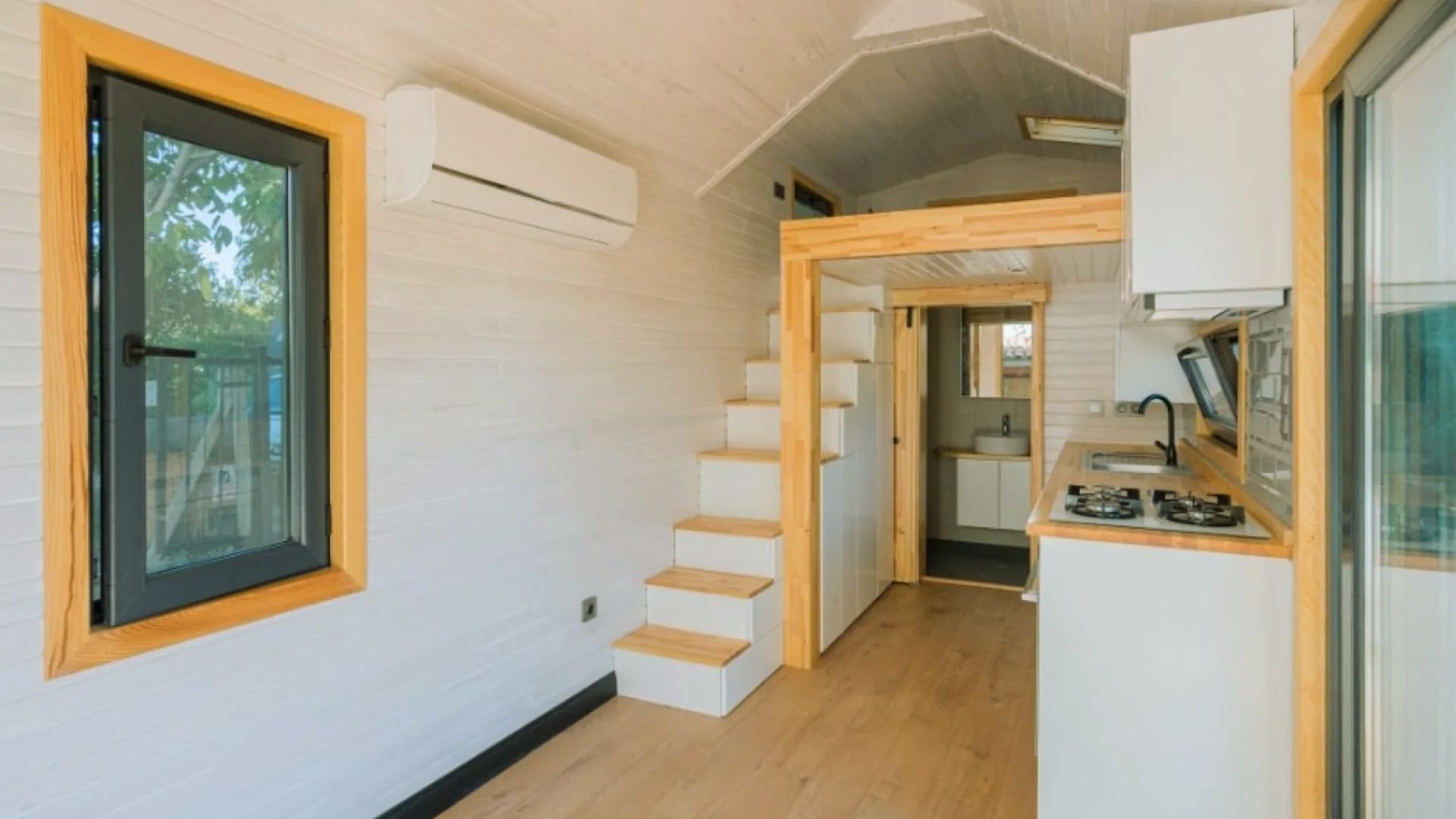 How shed-style homes feel larger - bright tiny house interior with vaulted ceiling, storage stairs and kitchen