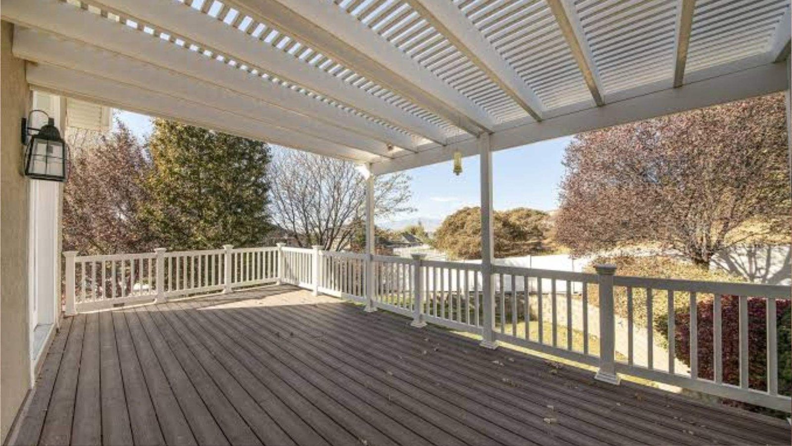 White vinyl pergola on elevated deck with stairs, lantern lights and railings under blue sky.