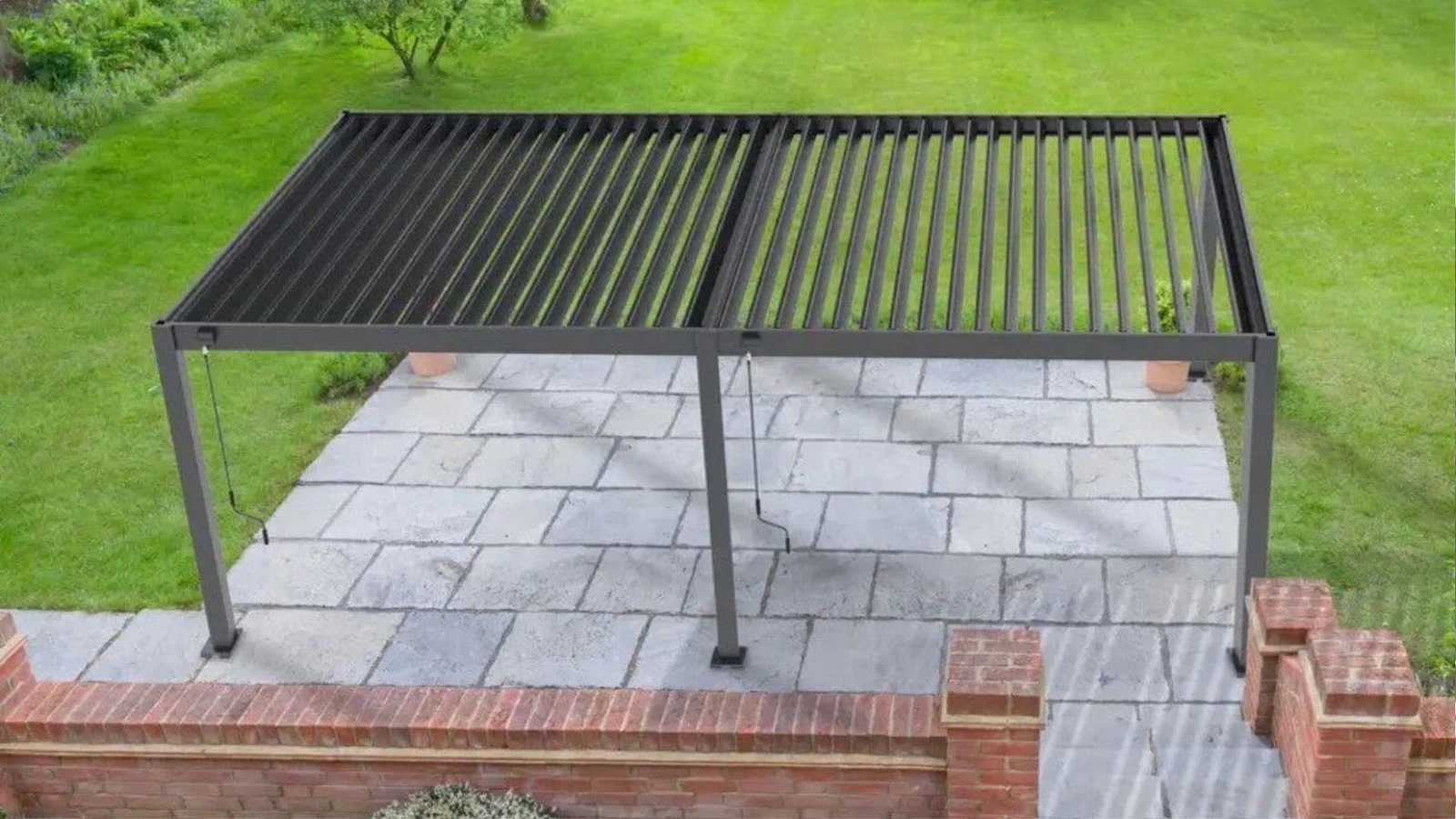 Modern black metal pergola with slatted roof over gray stone patio surrounded by green lawn