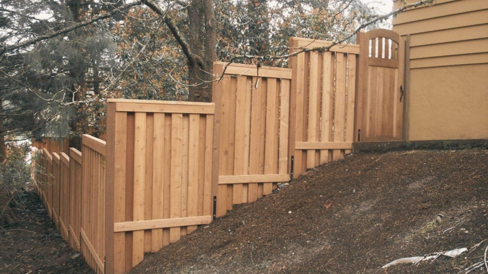 Wooden stepped privacy fence with gate installed on a steep sloped yard