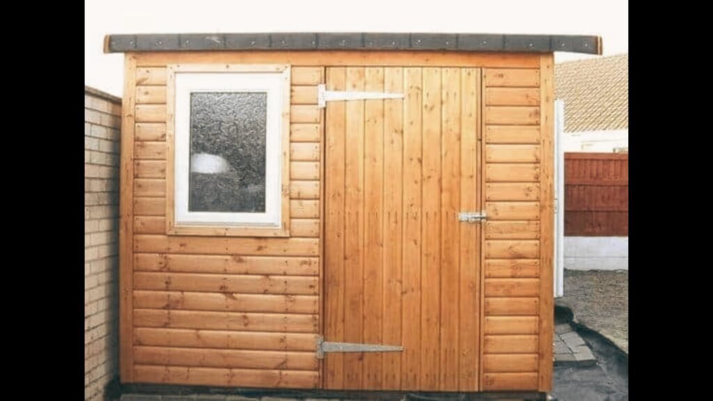 Wooden garden shed with a single timber door and a small white-framed window.