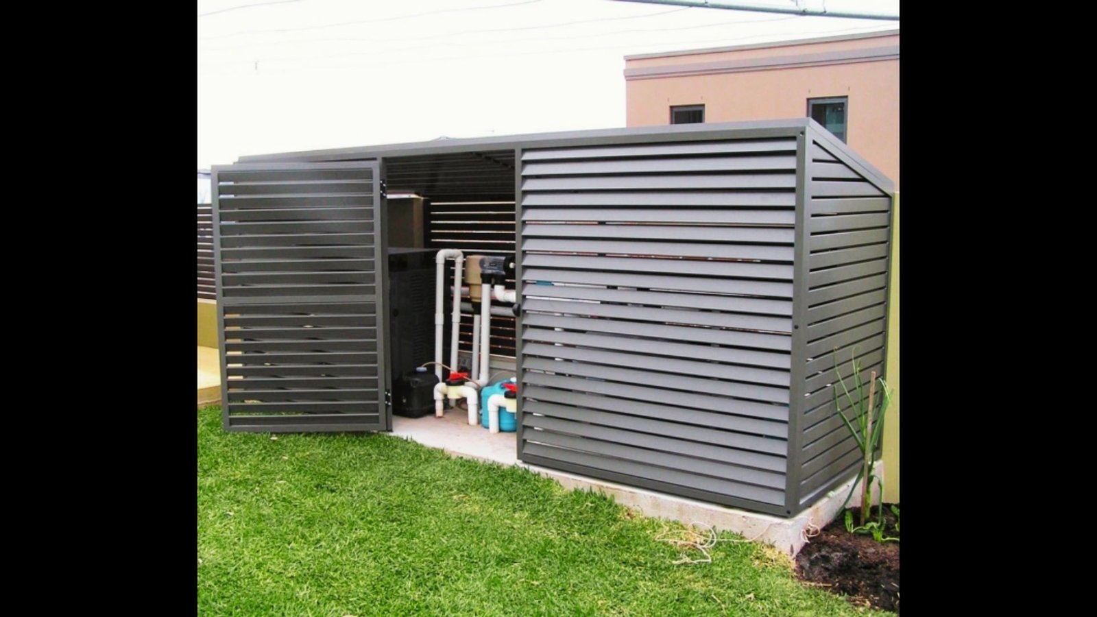A grey metal pool equipment enclosure with louvered slatted doors showing pool pumps and piping inside.
