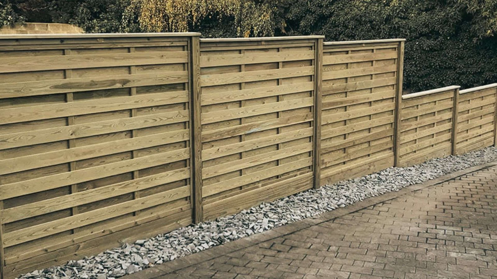 Wooden stepped fence panels on a slope with gravel border and brick paving