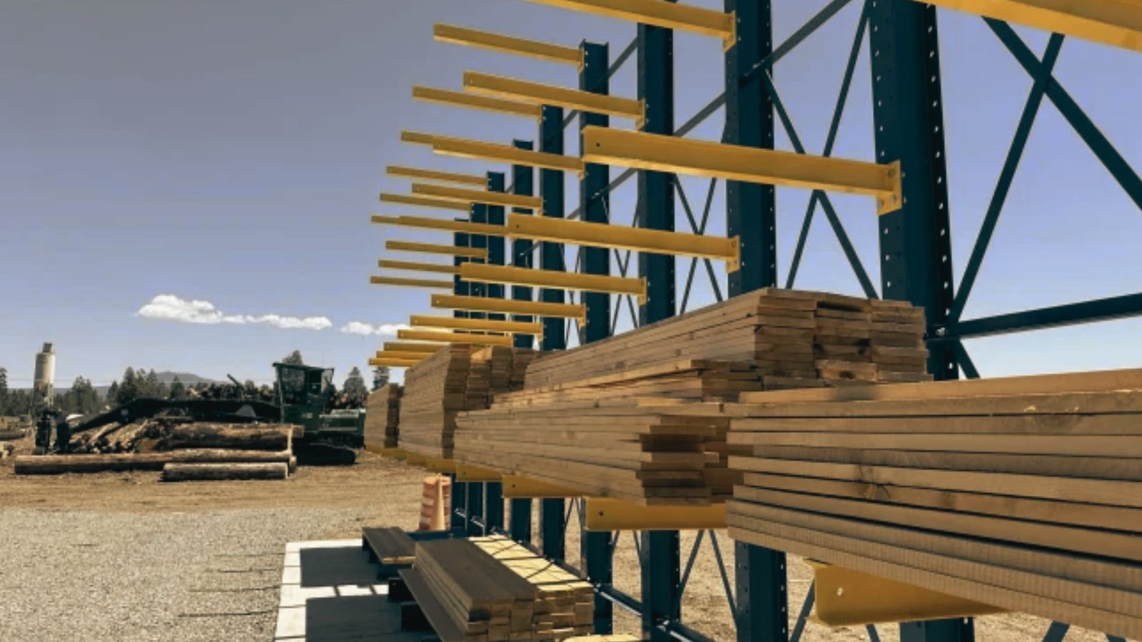 Yellow steel cantilever lumber rack arms holding stacked boards off the ground outdoors.
