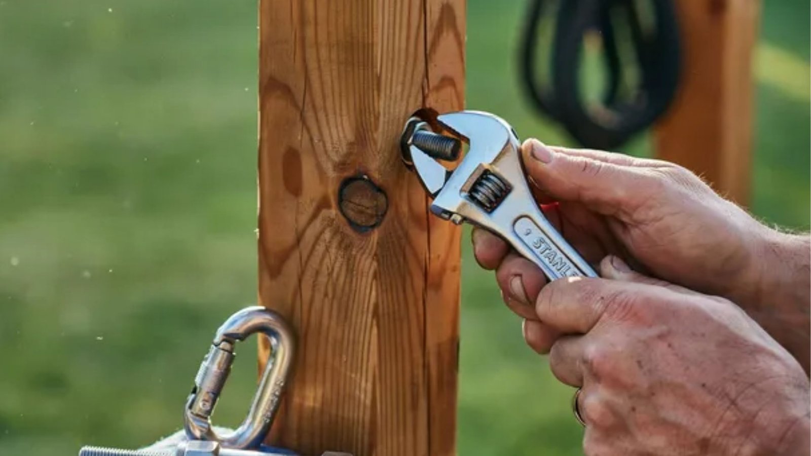 securing hardware to a wooden shade sail post using an adjustable wrench.