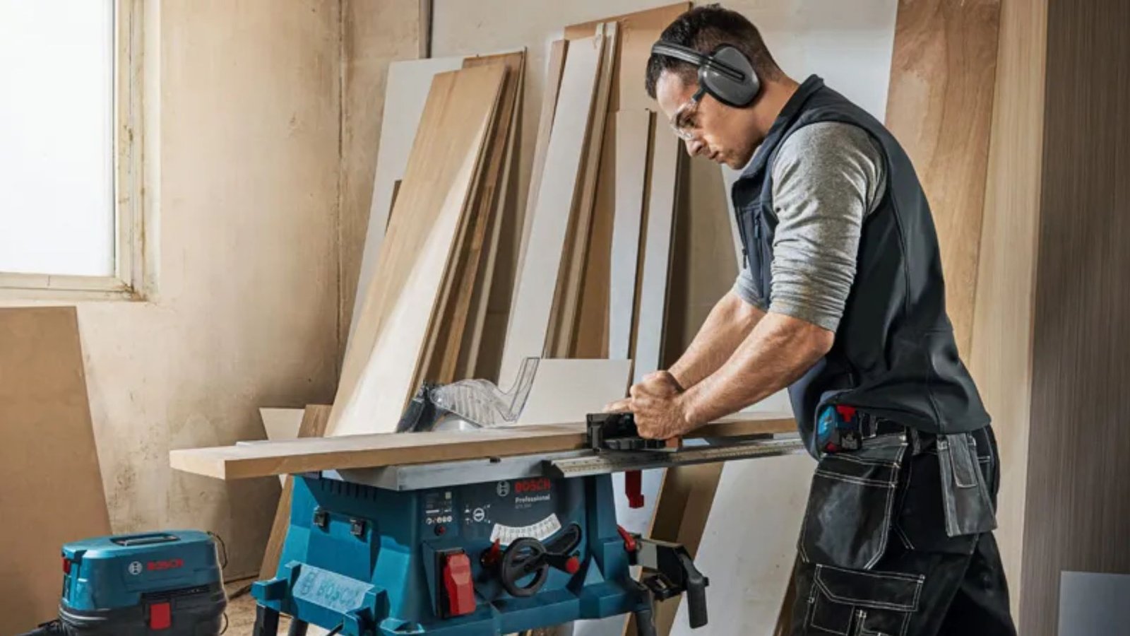 Man wearing ear muffs and safety glasses cutting a board on a table saw.