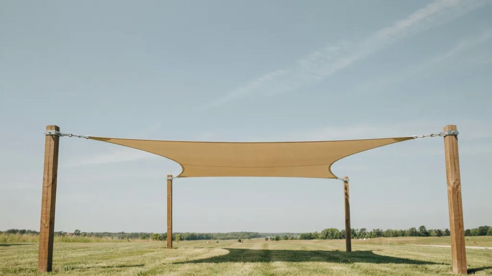 freestanding shade sail supported by four posts in an open backyard.