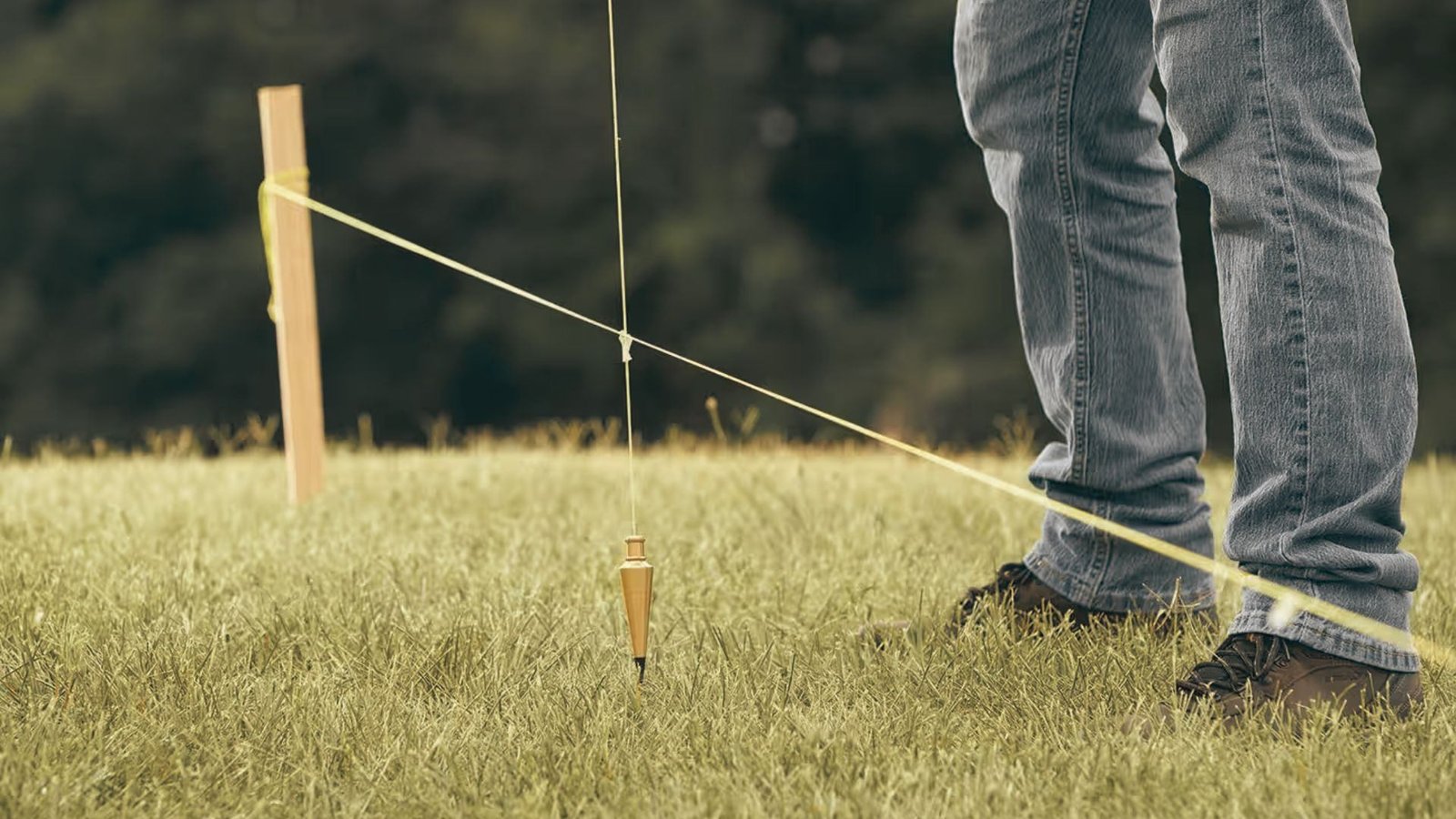 Marking fence post location on sloped grass with plumb bob and string line