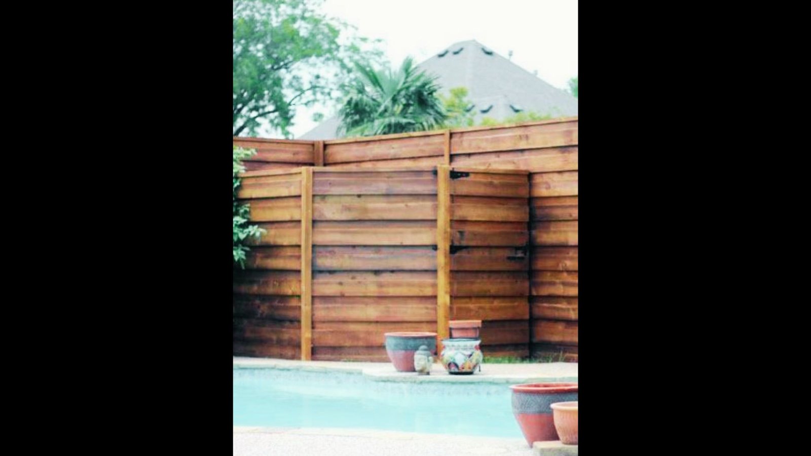 Horizontal wooden slat privacy screen enclosing a poolside area with decorative potted planters in front.