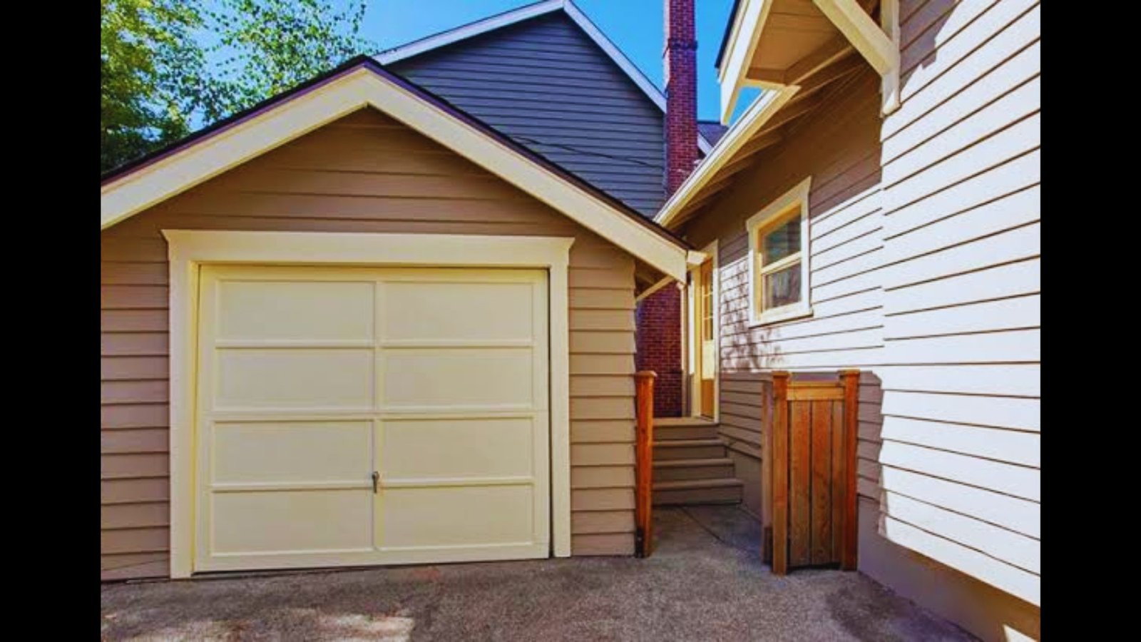 Single-car residential garage with a tan door and light siding attached to a house.