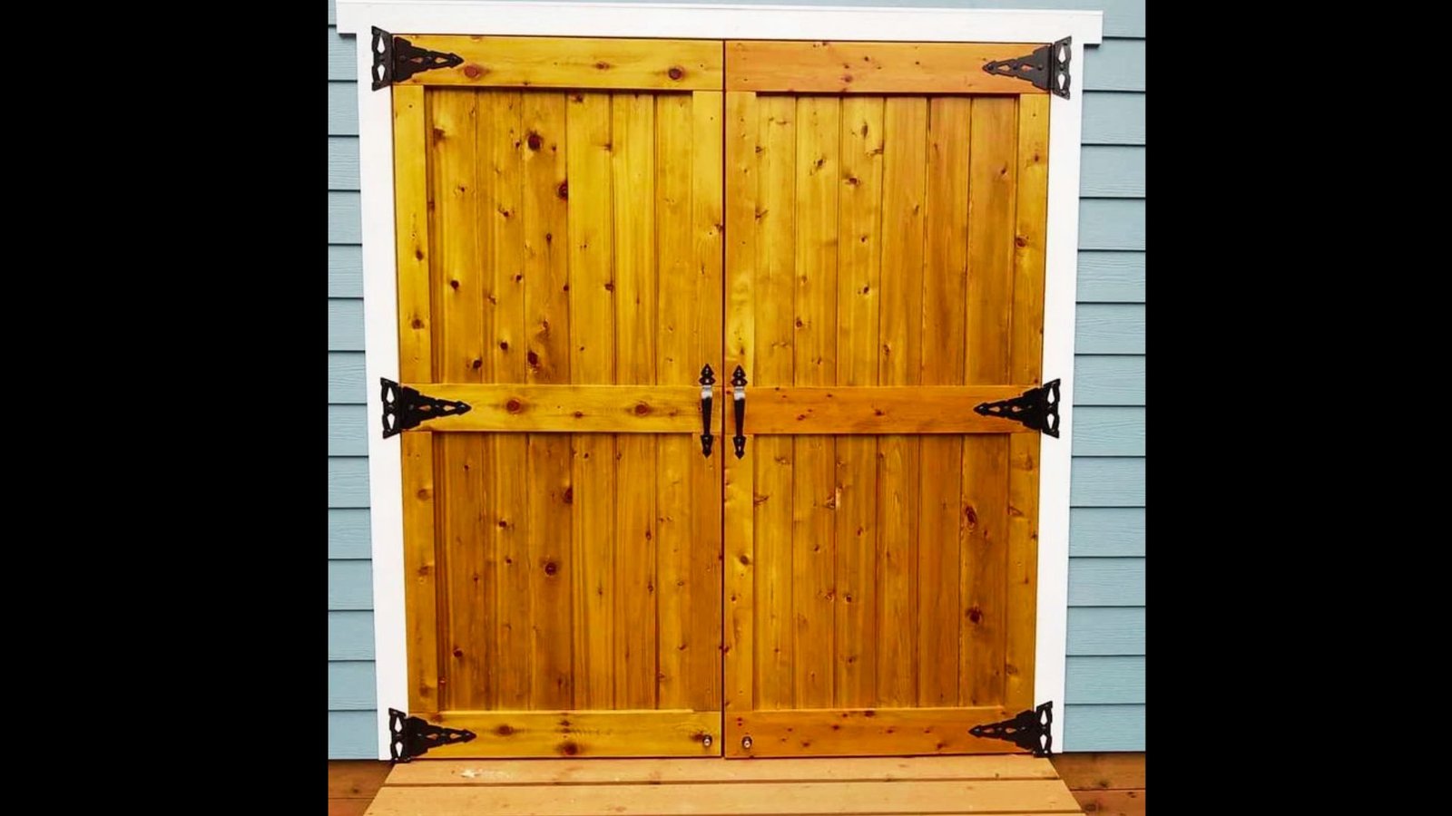 Rustic wooden double shed doors with black iron hinges and handles.