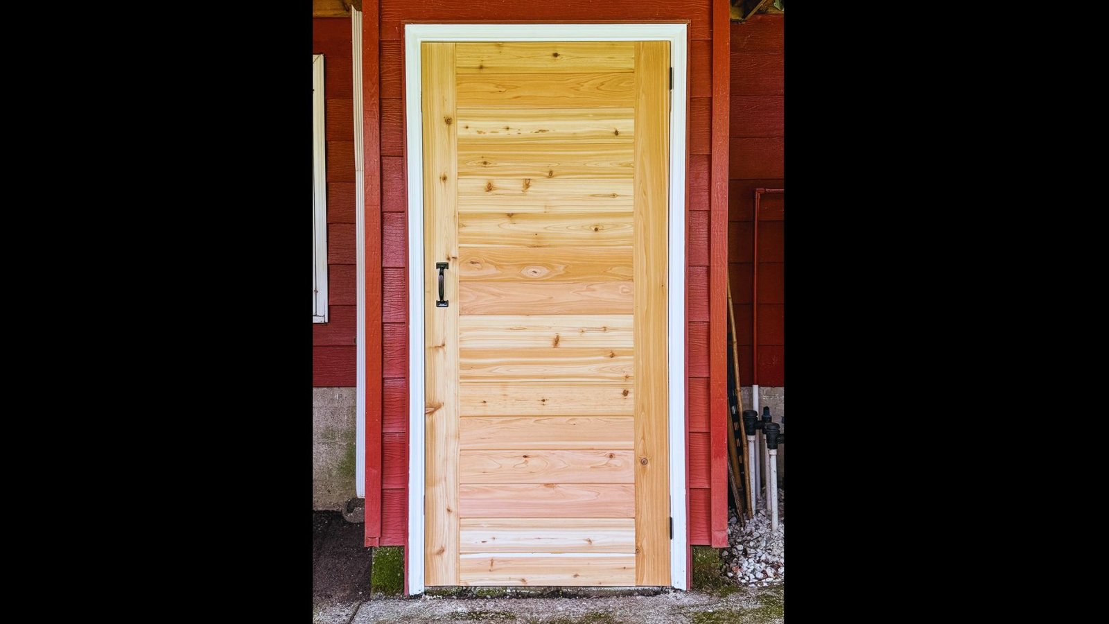 Light wood panel shed door with white framing on a red timber garden shed.