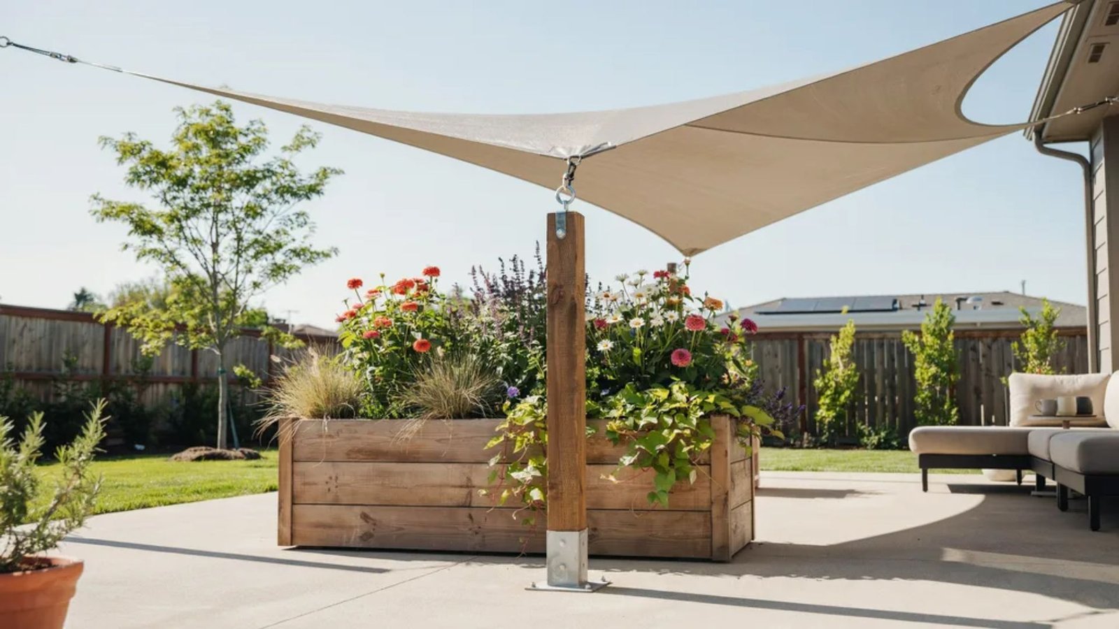 planter box with a sturdy shade sail post surrounded by flowers and greenery.