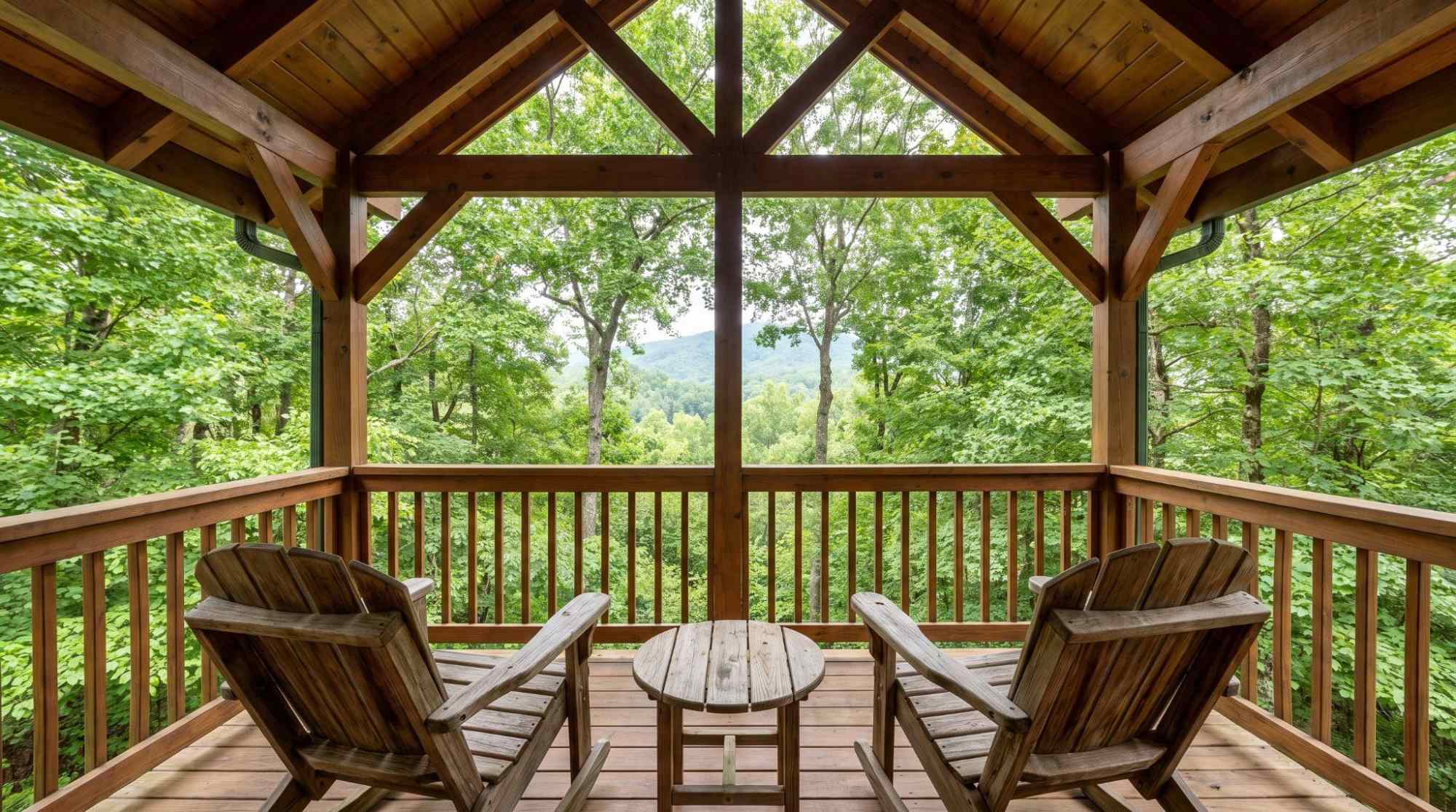 Covered wooden cabin deck with outdoor chairs, table, and surrounding greenery