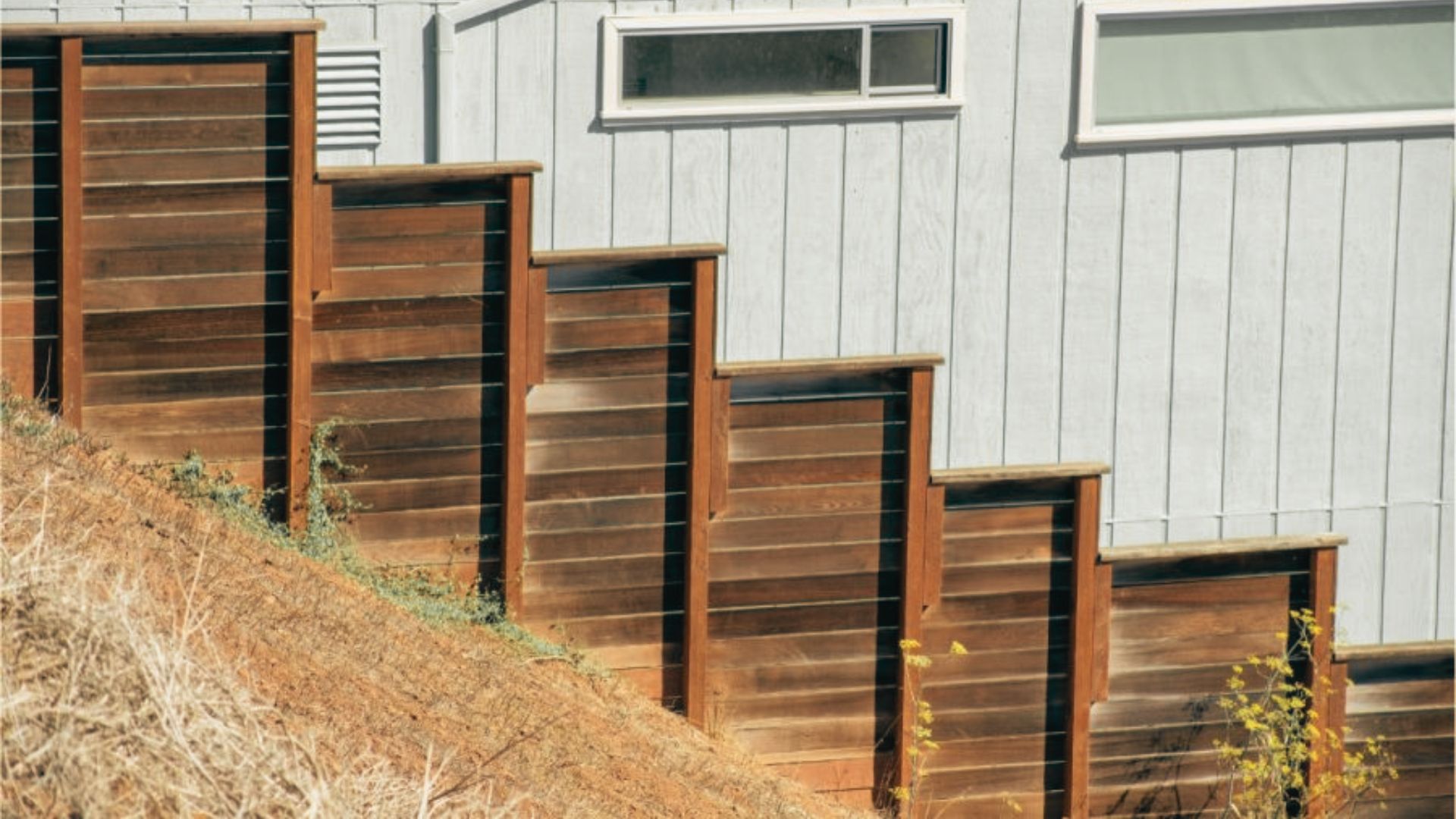 Stepped dark wood privacy fence on steep slope descending beside house