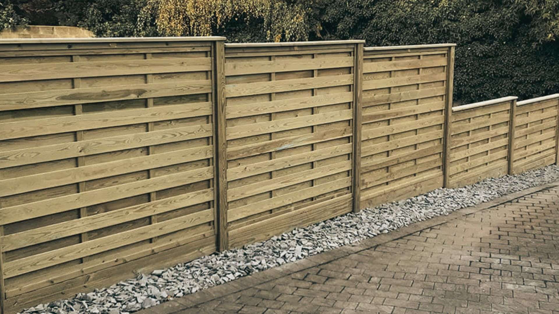 Wooden stepped fence panels on a slope with gravel border and brick paving