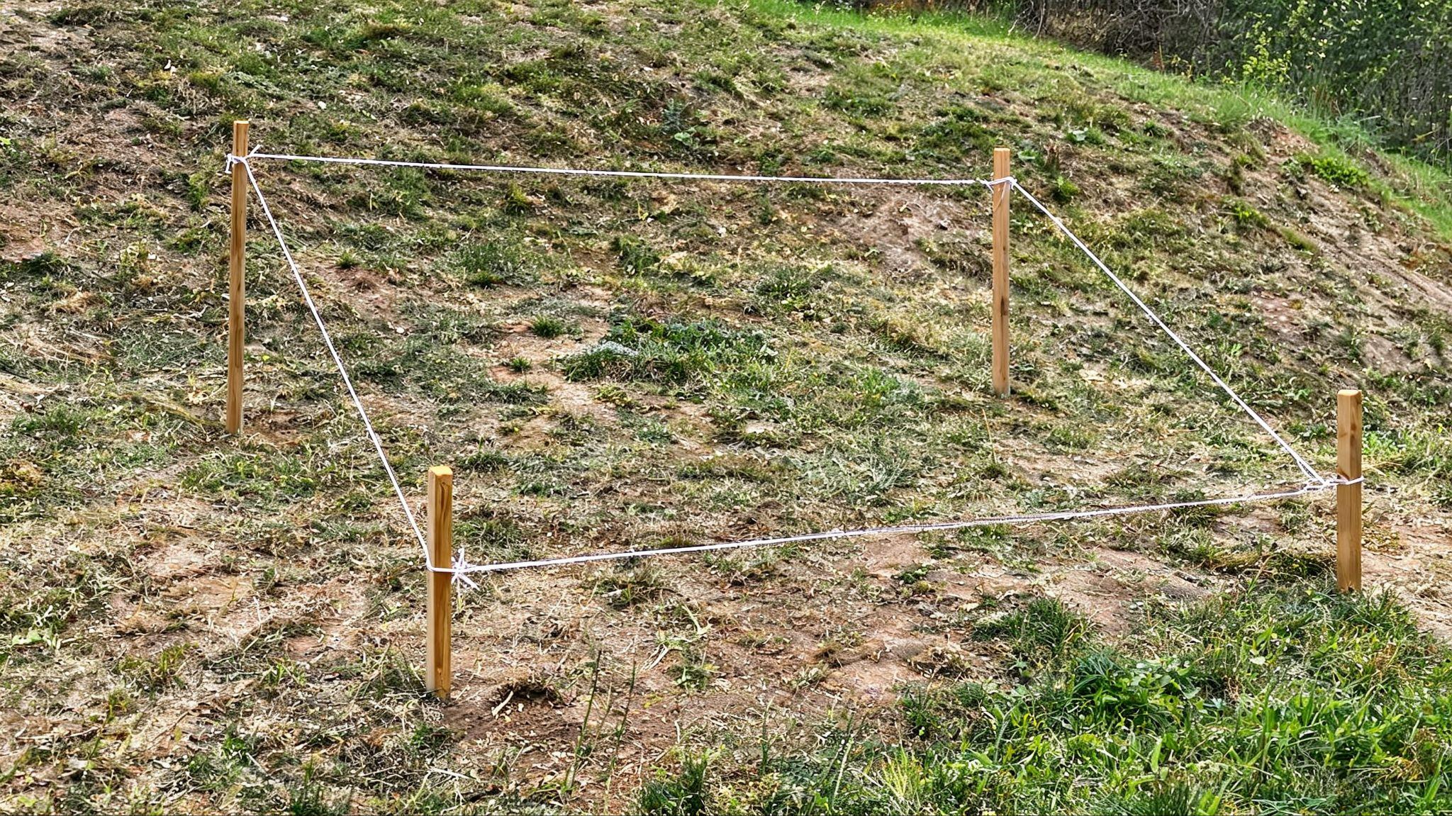 Shed footprint marked with stakes and string across a sloped yard
