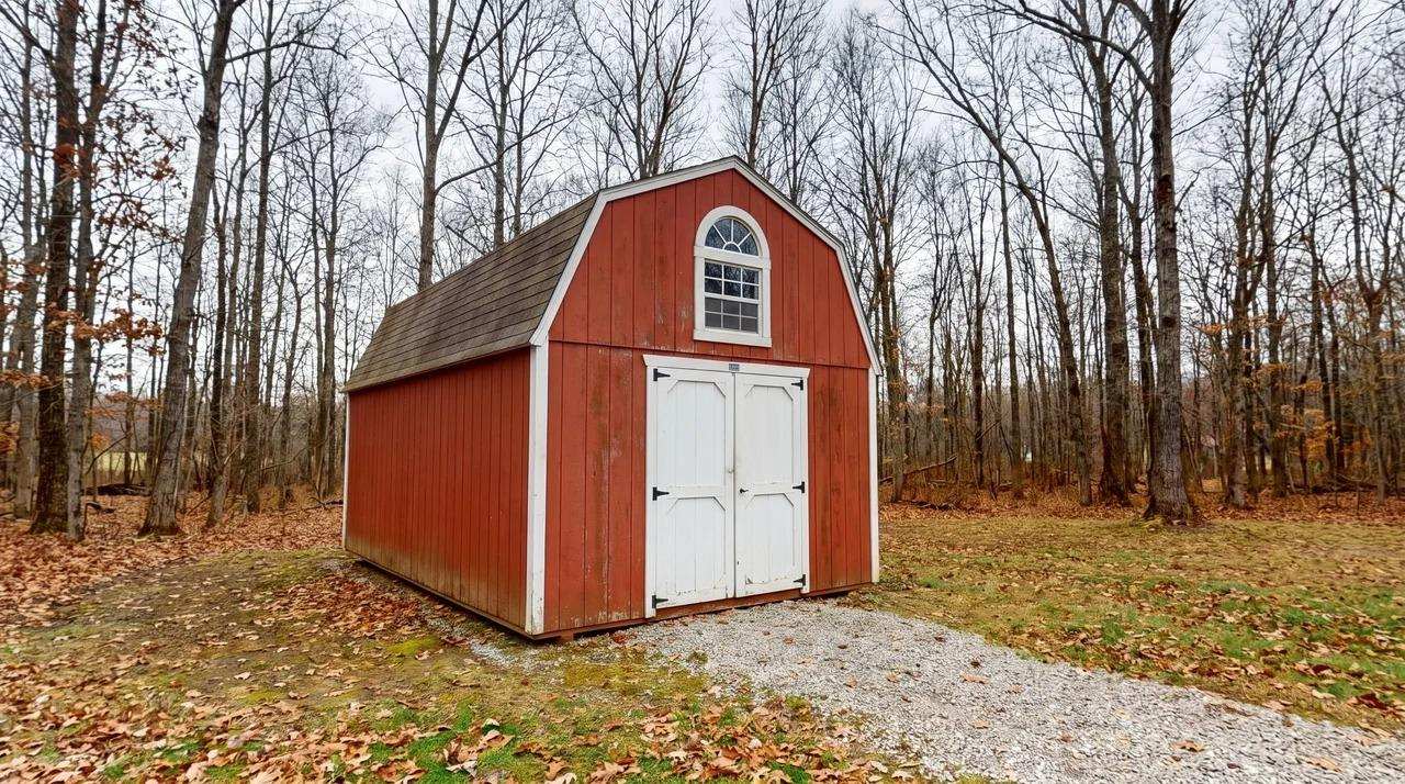 Red prefabricated shed with gambrel roof, white double doors, and arched window