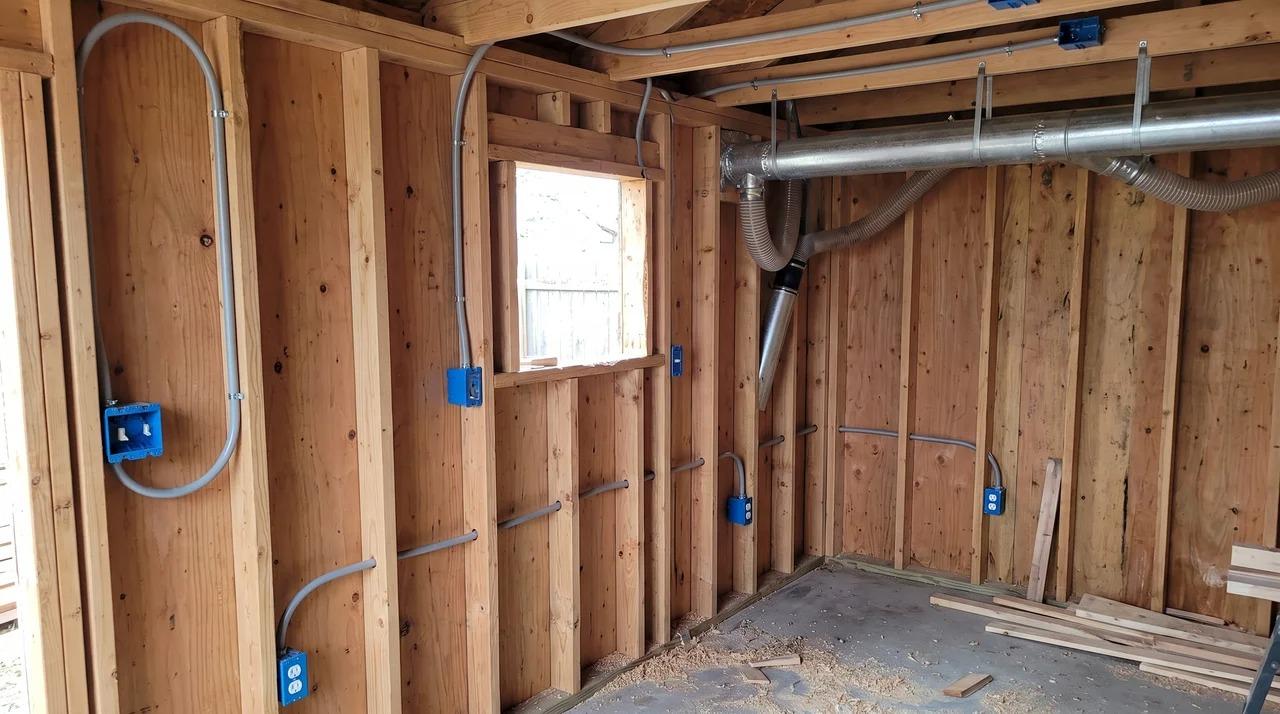 Unfinished shed interior with open studs, conduit, outlet boxes, and dust duct