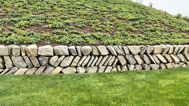 Knee-high retaining wall of stacked angular quarried boulders holding a planted slope above a mown lawnFile name-boulder-retaining-wall-slope