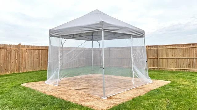 Pop-up canopy with mosquito netting walls and a weather-resistant rug on a mown backyard lawnFile name-pop-up-canopy-mesh-cabana