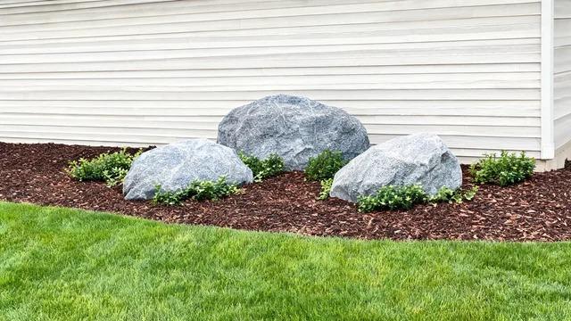 Cluster of three quarried boulders of different sizes with low green plants at their base in a front yard bedFile name-three-boulder-cluster-front-yard