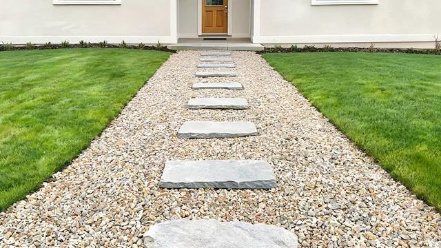 Flat flagstone stepping stones spaced evenly across gravel leading to a front doorFile name-stepping-stone-path-gravel