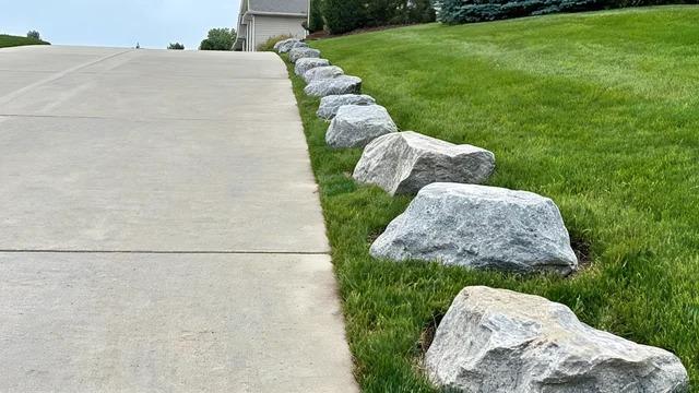 Quarried boulders spaced a few feet apart along an empty driveway edge beside a mown lawnFile name-boulders-driveway-edge-barrier