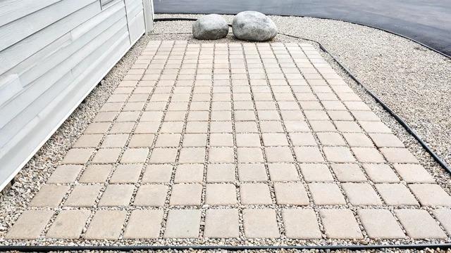 Pavers in straight lines with neutral gravel between them, steel edging, and two rounded boulders in a front yardFile name-pavers-gravel-boulders-front-yard