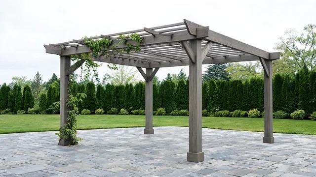 Open slatted gray-brown timber pergola with a green climbing vine on a bluestone patio beside a lawn and evergreen hedgesFile name-open-slat-pergola-between-gazebo-pavilion