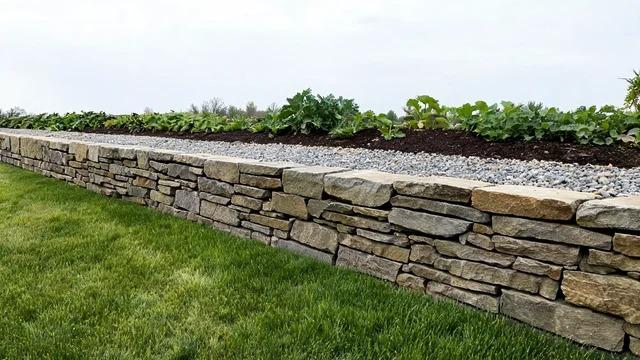 Low dry-stacked flat fieldstone wall with staggered joints around a raised front yard bed with low plantsFile name-dry-stacked-stone-border-wall