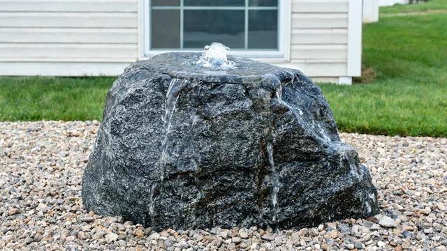 Drilled granite boulder with water bubbling over its sides into a gravel bed in a front yardFile name-bubbling-granite-boulder-water-feature