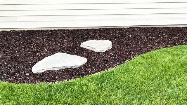 Dark mulch bed with two light fieldstones set in it beside a mown front lawn